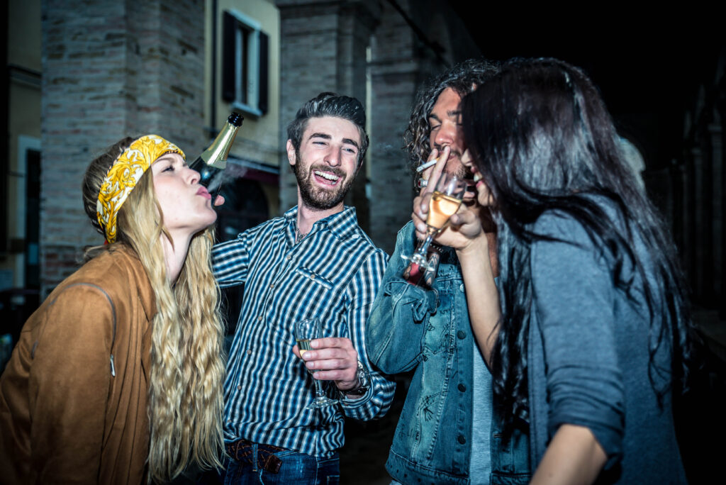 A group of people drinking and smoking, symbolizing experimentation with substances. This image illustrates the phase where curiosity and peer influence may lead to regular substance use, potentially paving the way towards addiction.