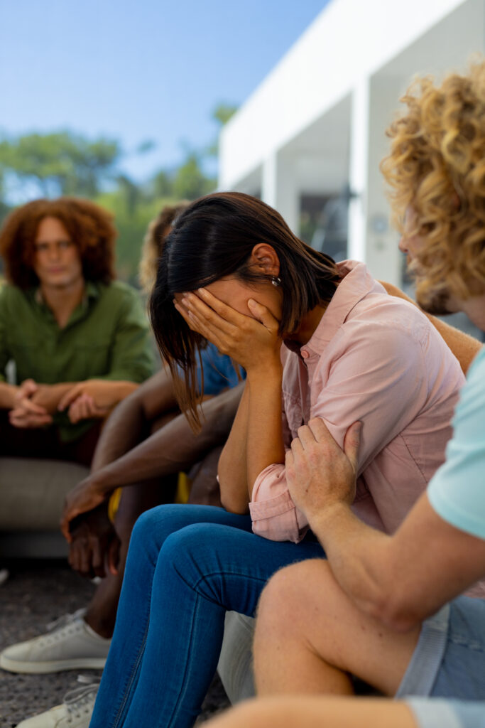 Image of a woman with her head in her hands being comforted by a man in a support group setting, illustrating the emotional support and compassion found within addiction support groups.