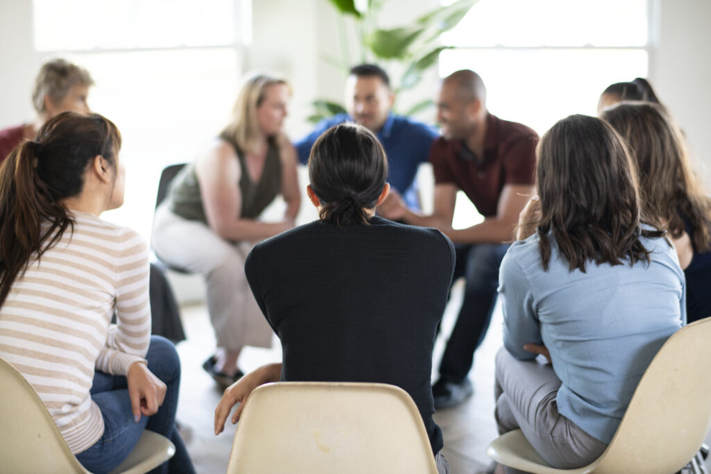 Image of a diverse group of individuals gathered in a support group setting, engaged in conversation and offering support to each other. Their body language reflects empathy and understanding, highlighting the importance of peer support in mental health and addiction recovery.