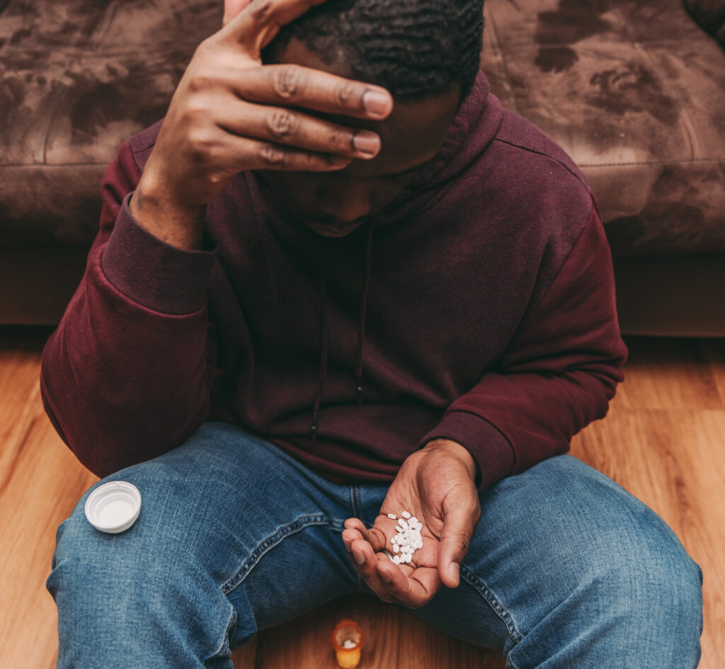 A man holding a handful of pills with his hand on his head, deep in contemplation. This image represents the internal conflict faced by individuals grappling with addiction concealment, a red flag signaling a growing attachment to substances or behaviors.