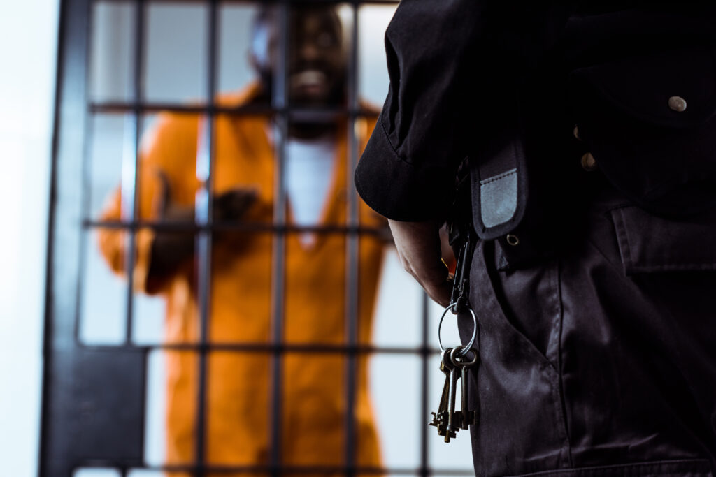 A corrections officer stands beside a prisoner behind bars, representing the challenges faced within the correctional system. This image accompanies the section of the blog discussing the challenges correctional officers face.




