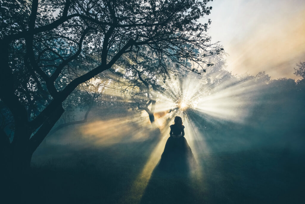Woman standing in forest with sunlight filtering through, embodying spirituality's impact on mental health and addiction recovery.