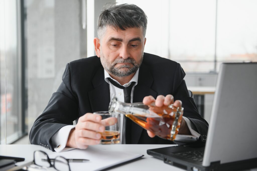 Man discreetly drinking alcohol at his office desk.