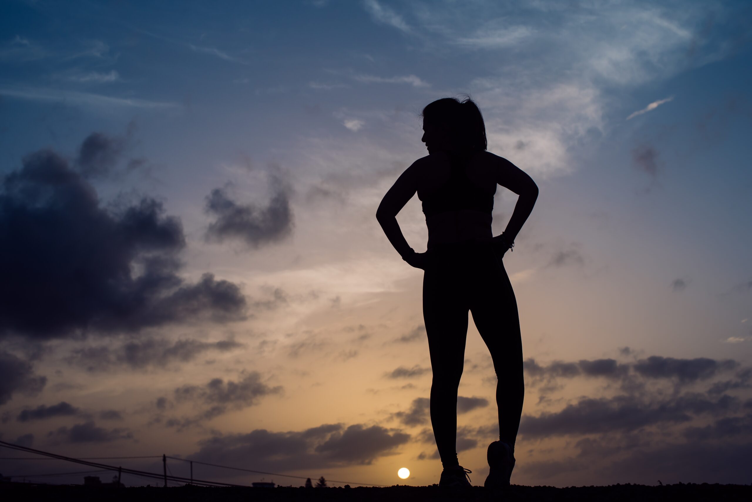 Silhouette of a woman against a sunset sky, symbolizing the interplay of discipline and recovery in her journey towards renewal.