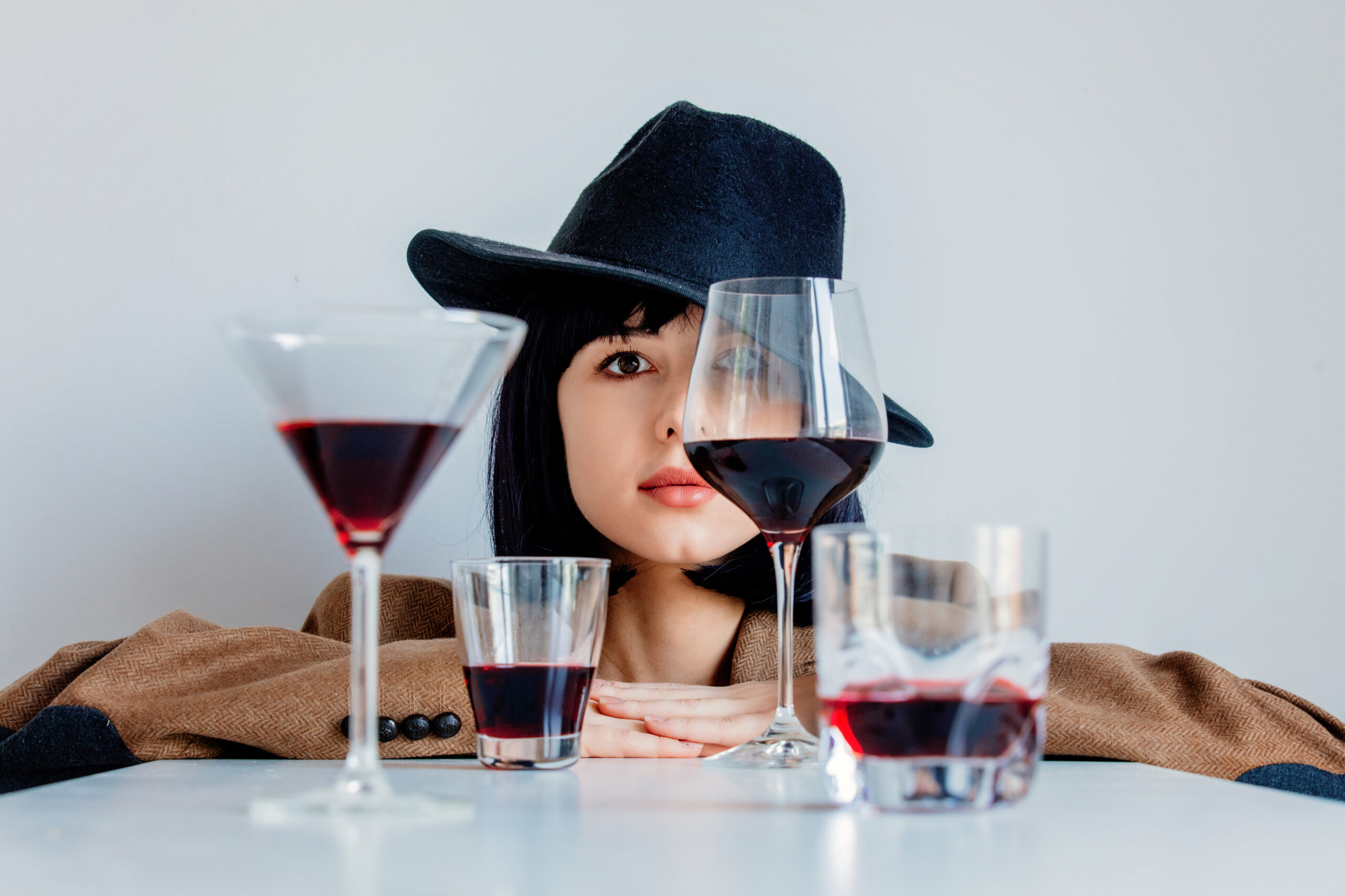 A thoughtful woman examines multiple glasses of wine placed in a row, symbolizing the search for signs of alcoholism.
