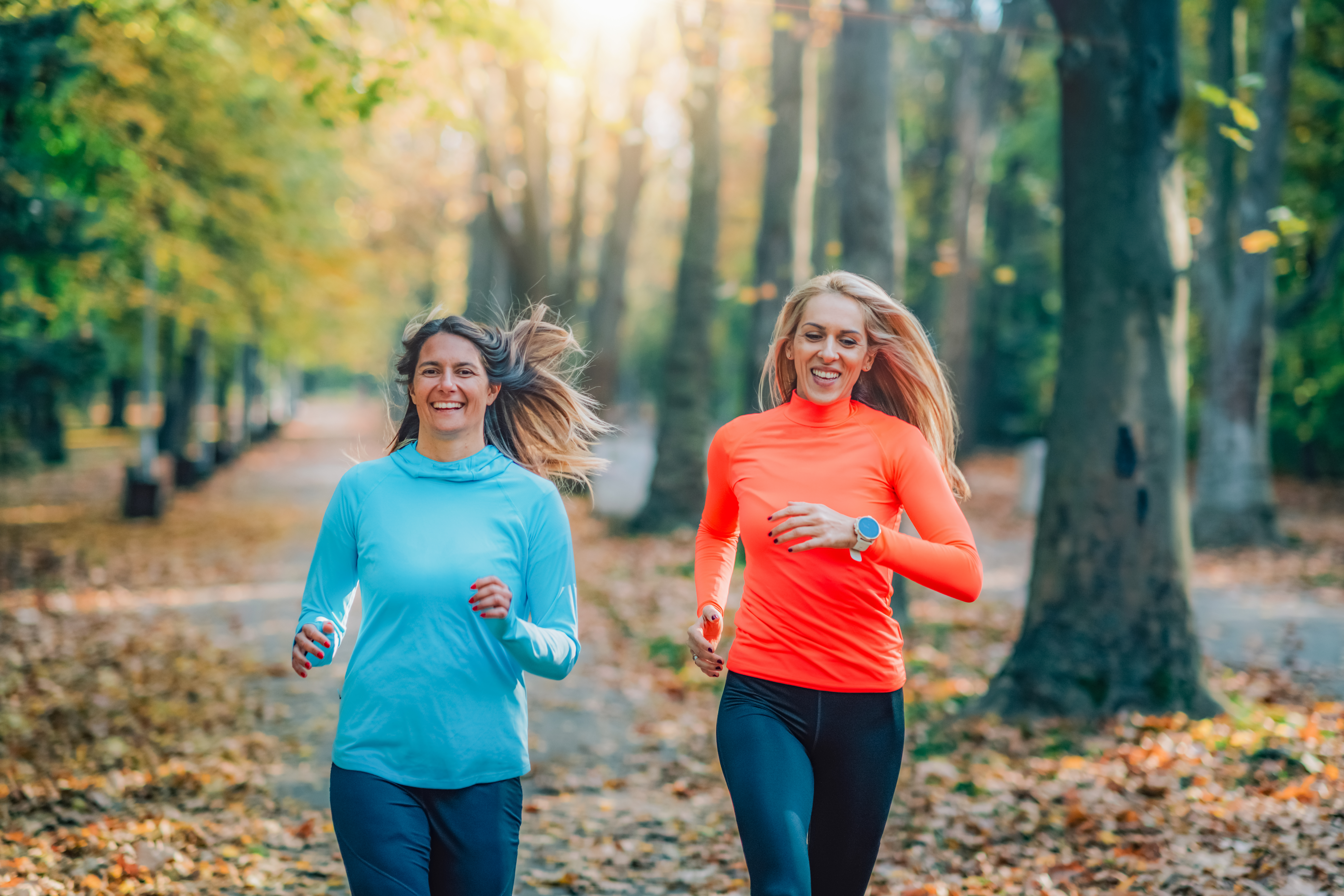 Two smiling women jogging in a park, representing the positive impact of physical activity on mental health.