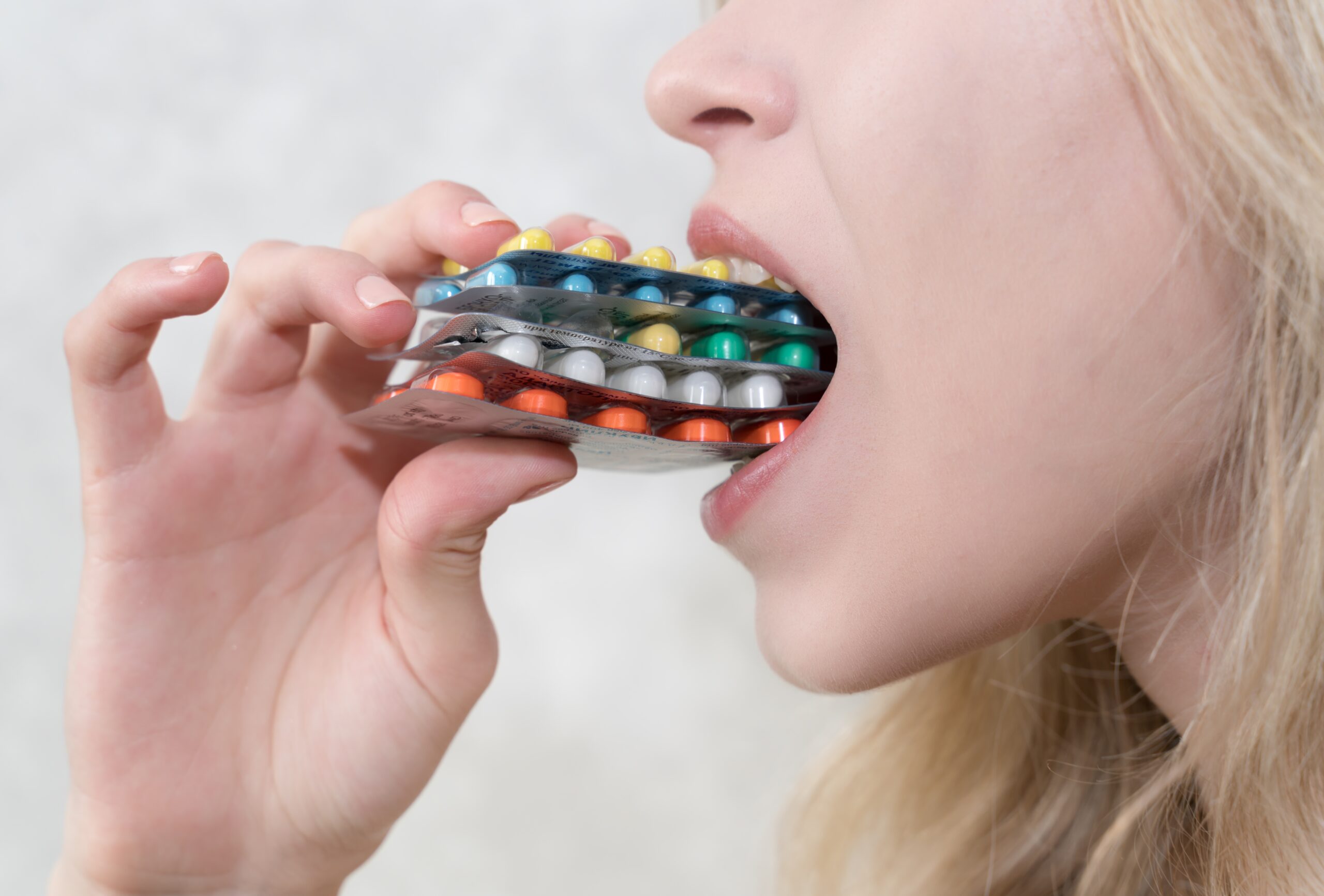 woman overwhelmed by mental health issues, attempting to take multiple packets of pills at once, highlighting the challenges of medication management.