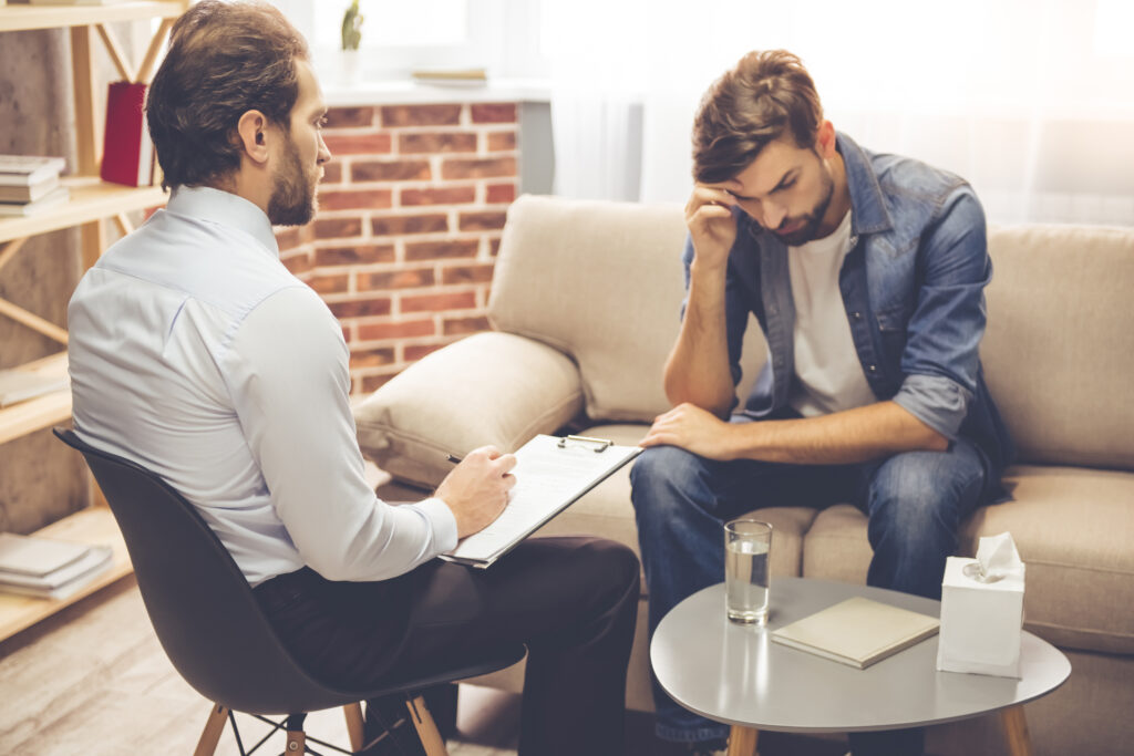  A man sitting in a therapist's office, seeking help for addiction recovery, highlighting treatment options for substance abuse and behavioral addictions.