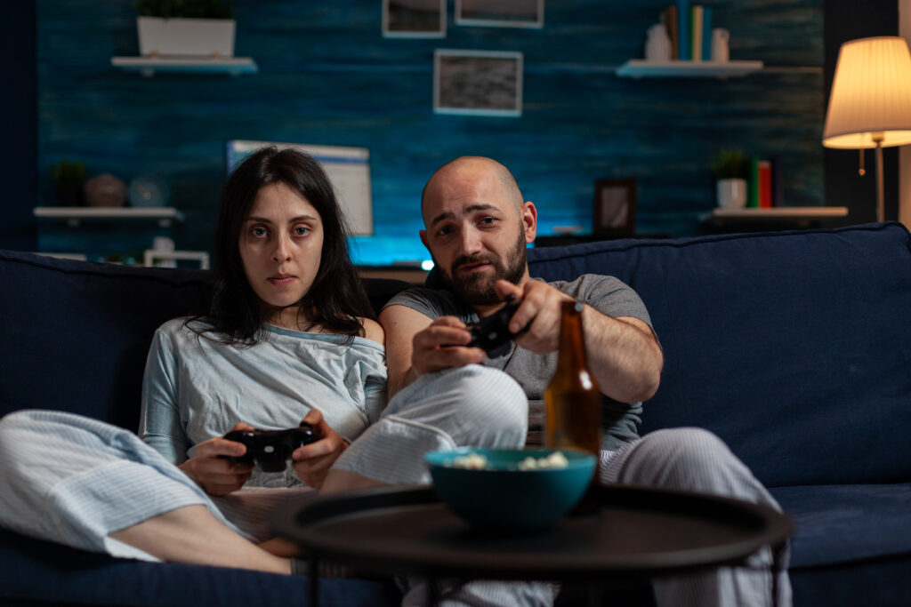 A man and woman sitting on a couch intensely playing video games, illustrating behavioral addiction and highlighting different types of addiction.