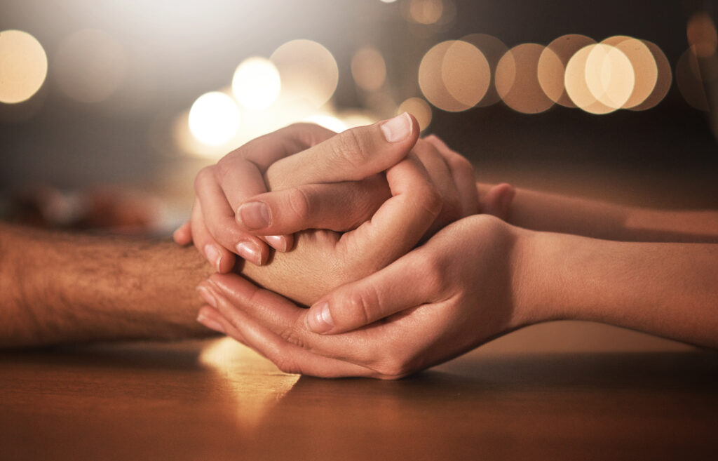 Two people holding hands with lights in the background, symbolizing how to help a loved one through recovery and provide support during the holidays.