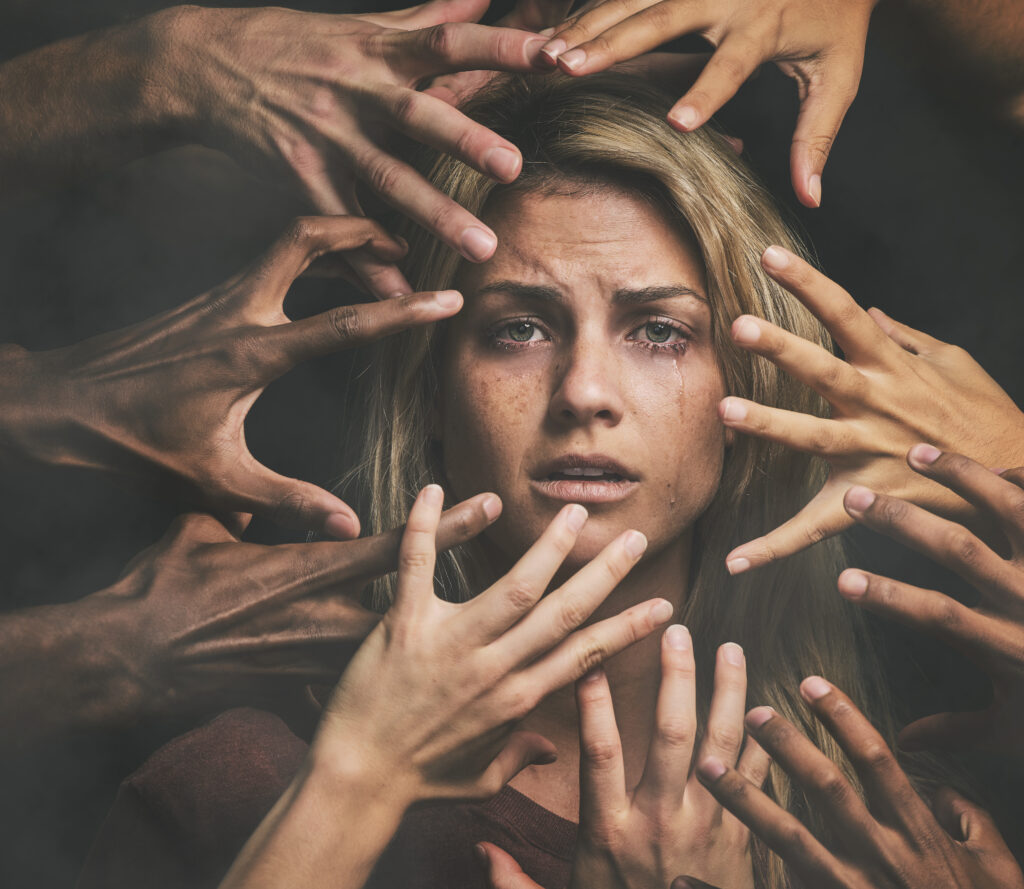 A traumatized woman surrounded by hands reaching toward her face, symbolizing the struggle of addiction and the path to trauma recovery