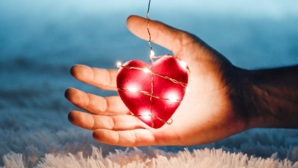 A hand holding a glowing heart wrapped in lights, symbolizing how to help a loved one struggling with addiction and mental health challenges during the holidays.