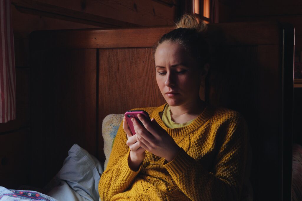 Teen using a smartphone in a dark room, representing overstimulation and isolation