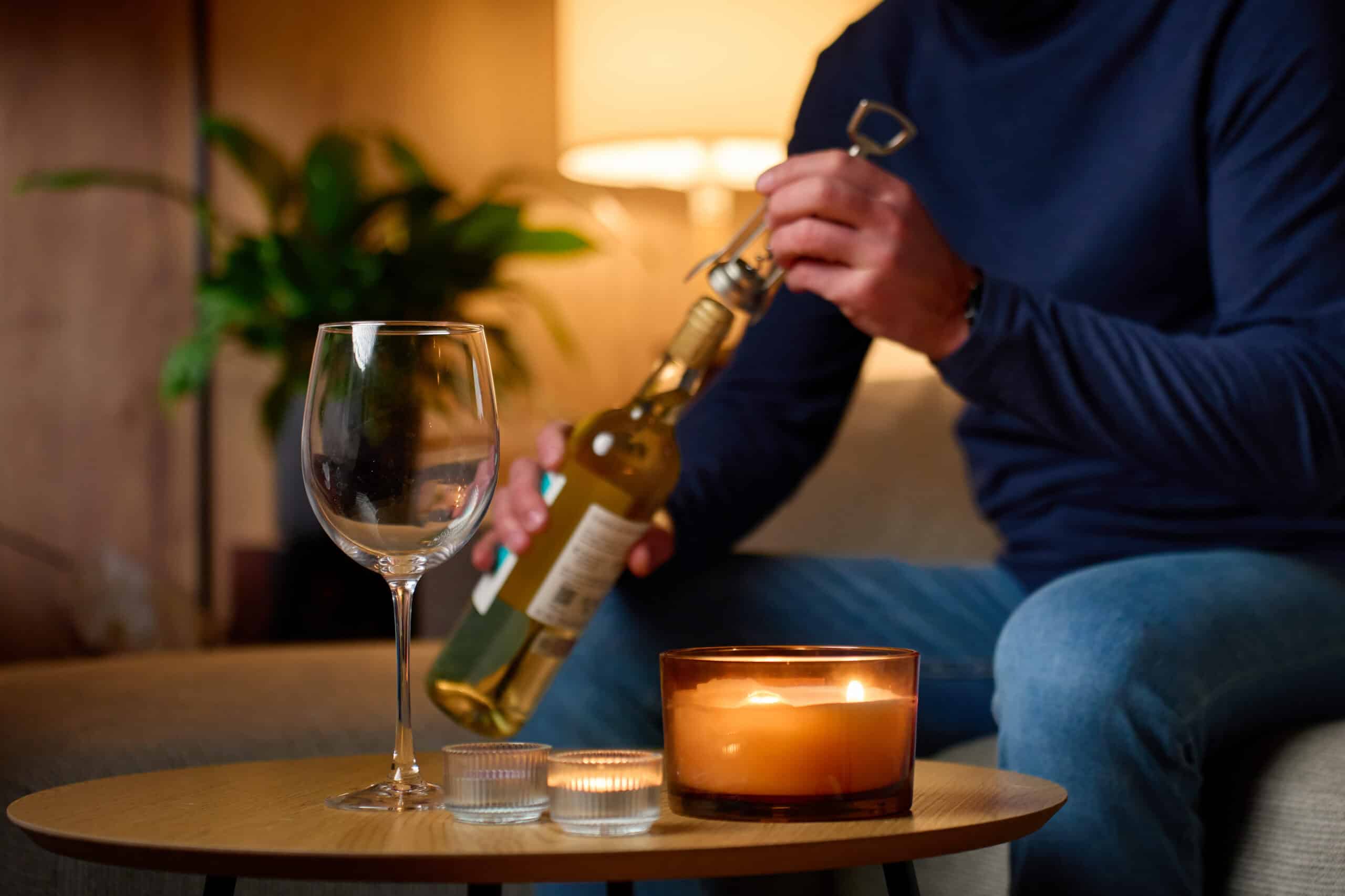 A man opens a bottle of wine alone at home in the evening.